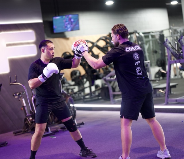 Baki holding focus mitts for a boxing student in the gym