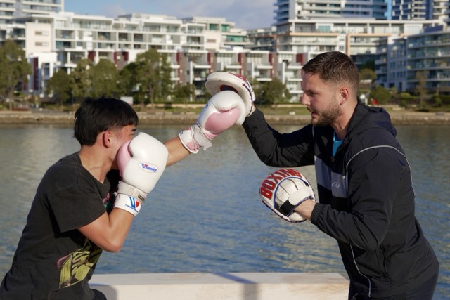Baki coaching a boxing student through outdoor padwork