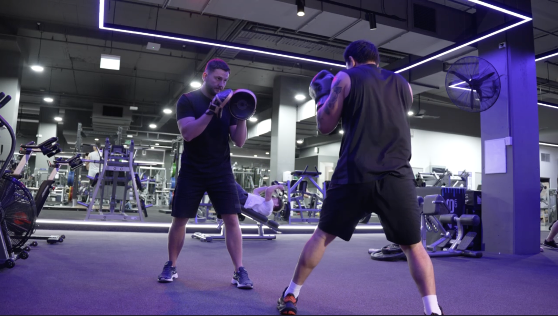 Coach Baki holding focus mitts for a boxer in the gym